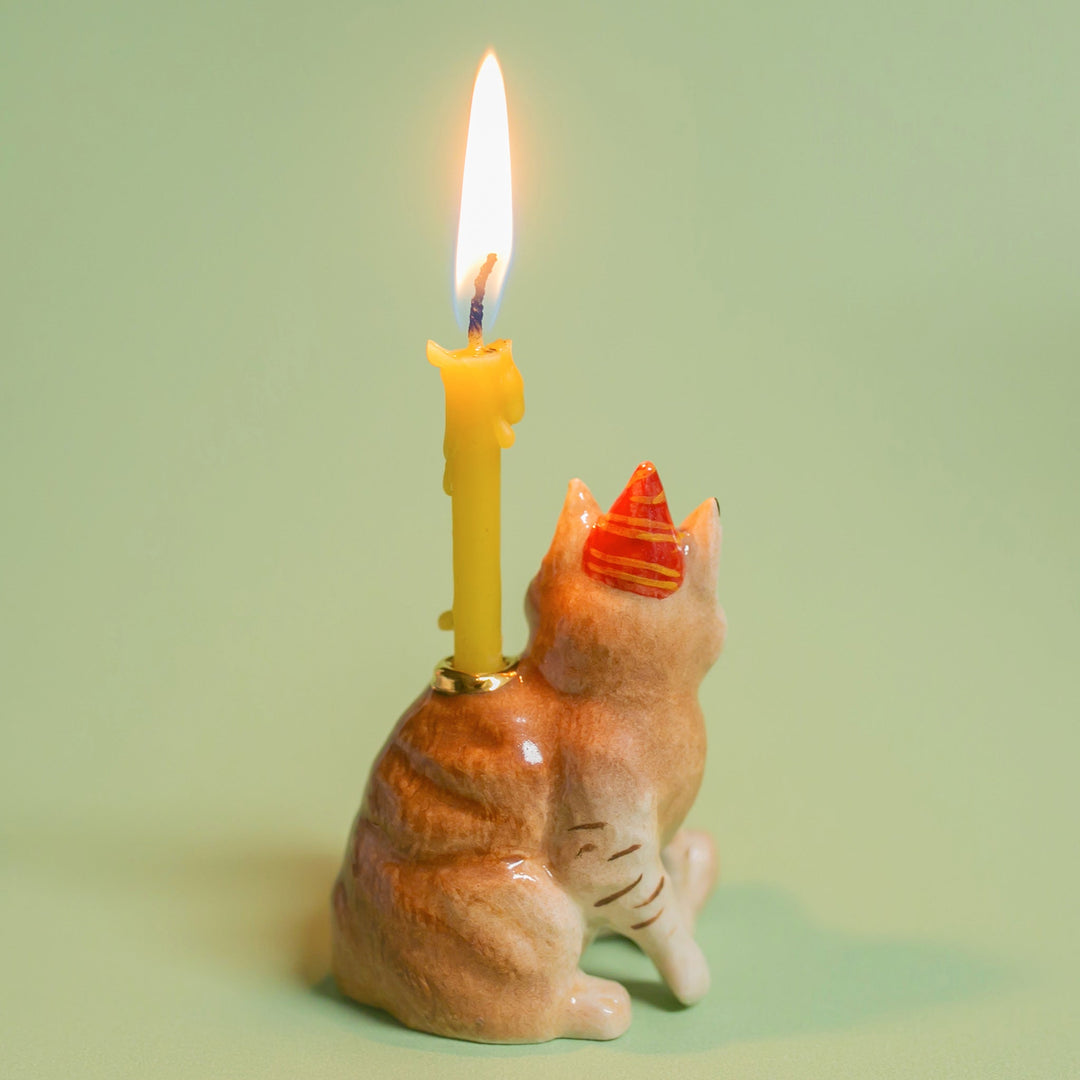 Orange tabby cat porcelain candle holder in a party hat holding a lit birthday candle for a cat lover's birthday cake