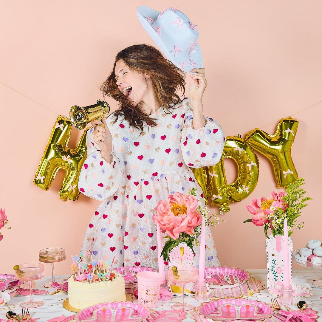 Woman in a cowboy hat holding the gold megaphone at a birthday party with gold letter balloons