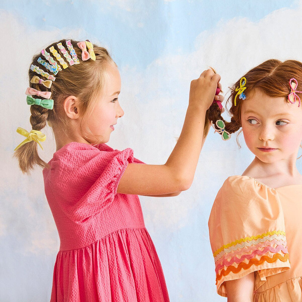 Child wearing pastel floral wavy hair clips along a braid while styling another child’s hair.