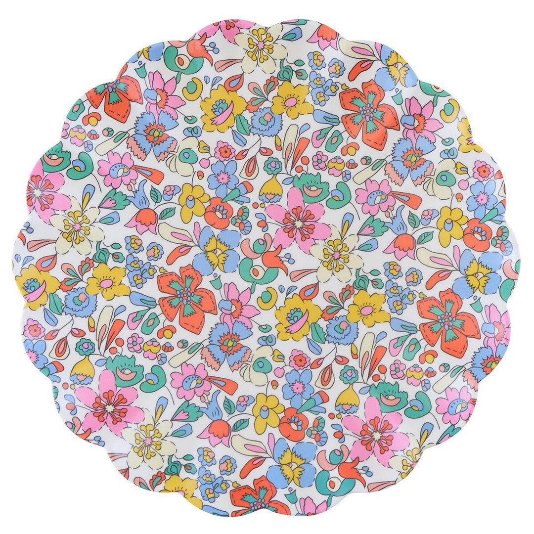 Scalloped reusable melamine plate with stylized pink, orange, blue and yellow Liberty flowers on white.
