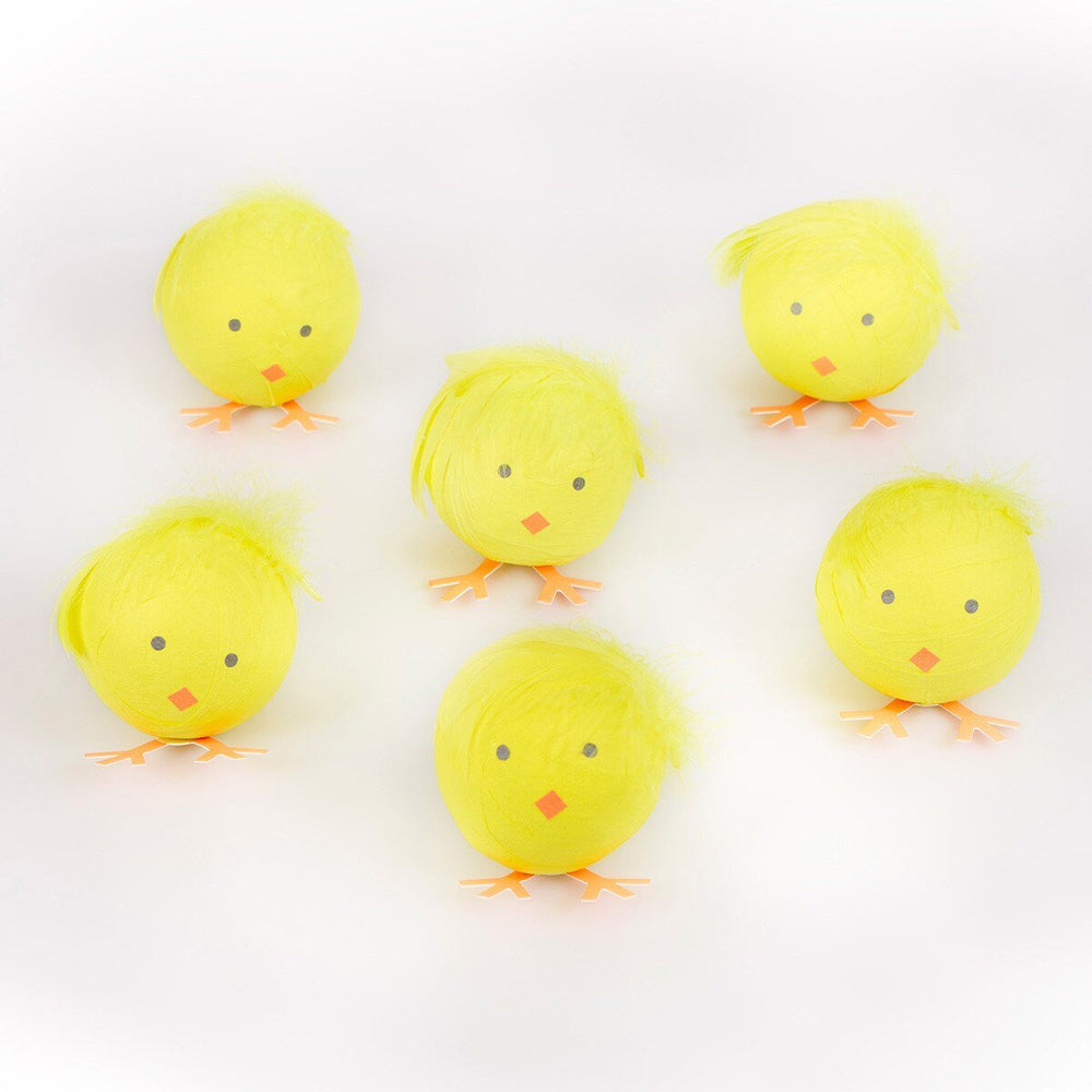 Six round yellow chick surprise balls with black eyes, orange beaks and orange feet arranged against white.