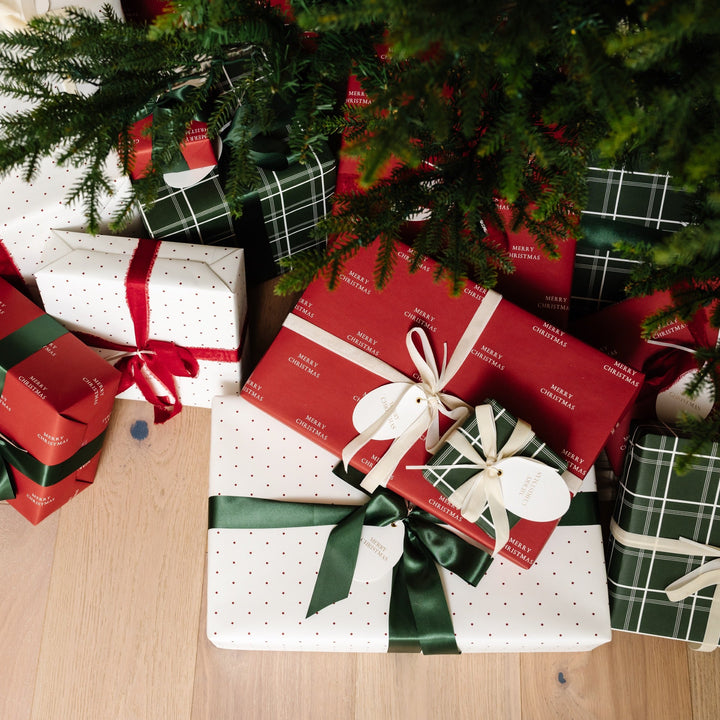 Wider view of red, plaid, and polka dot gifts on a wood floor beneath Christmas tree branches