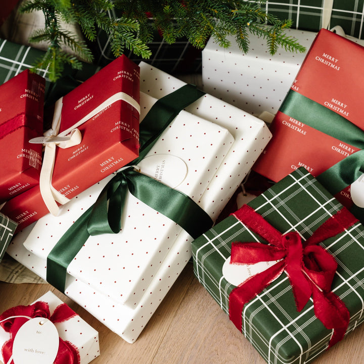Plaid and polka dot wrapped presents with red and green bows tucked under a Christmas tree