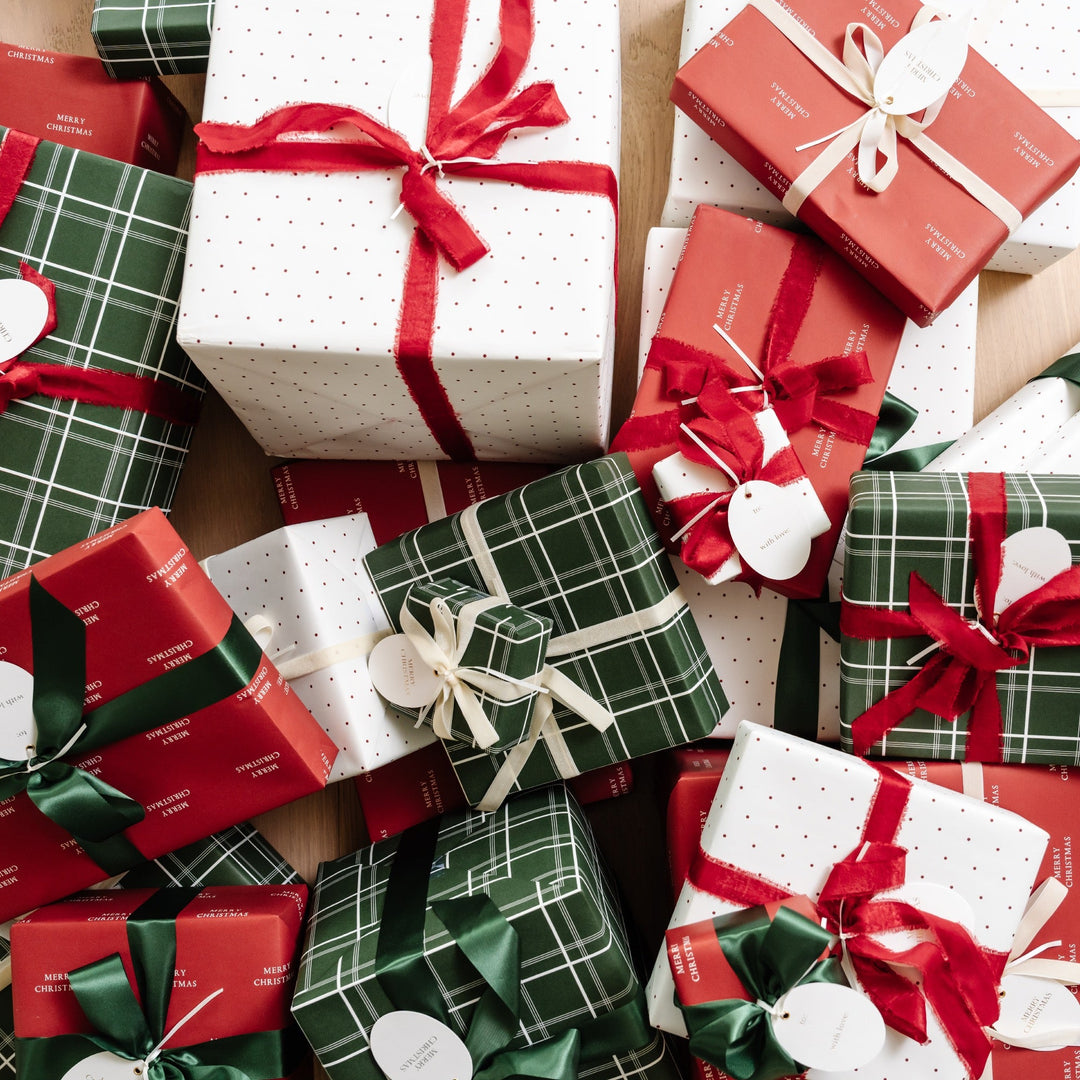 Overhead pile of Christmas gifts in green plaid, polka dot, and Merry Christmas paper with red bows