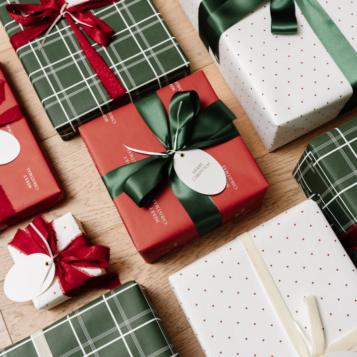 Top-down rows of plaid, red, and dotted Christmas presents with green satin bows on wood