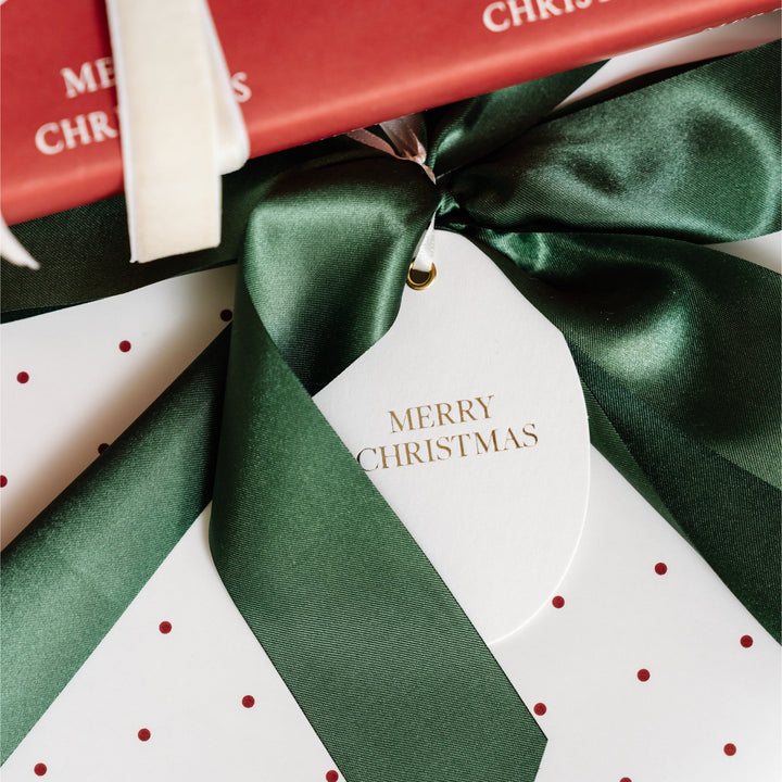 Close-up of a green satin bow and gold foil Merry Christmas tag on red polka dot gift wrap