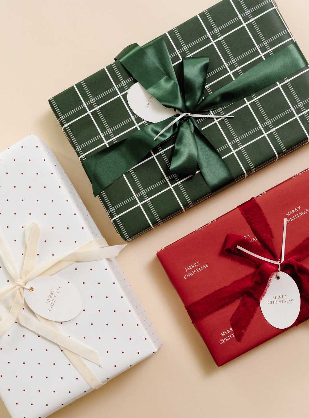 Gifts in green windowpane plaid, red polka dot, and red Merry Christmas paper with bows on cream