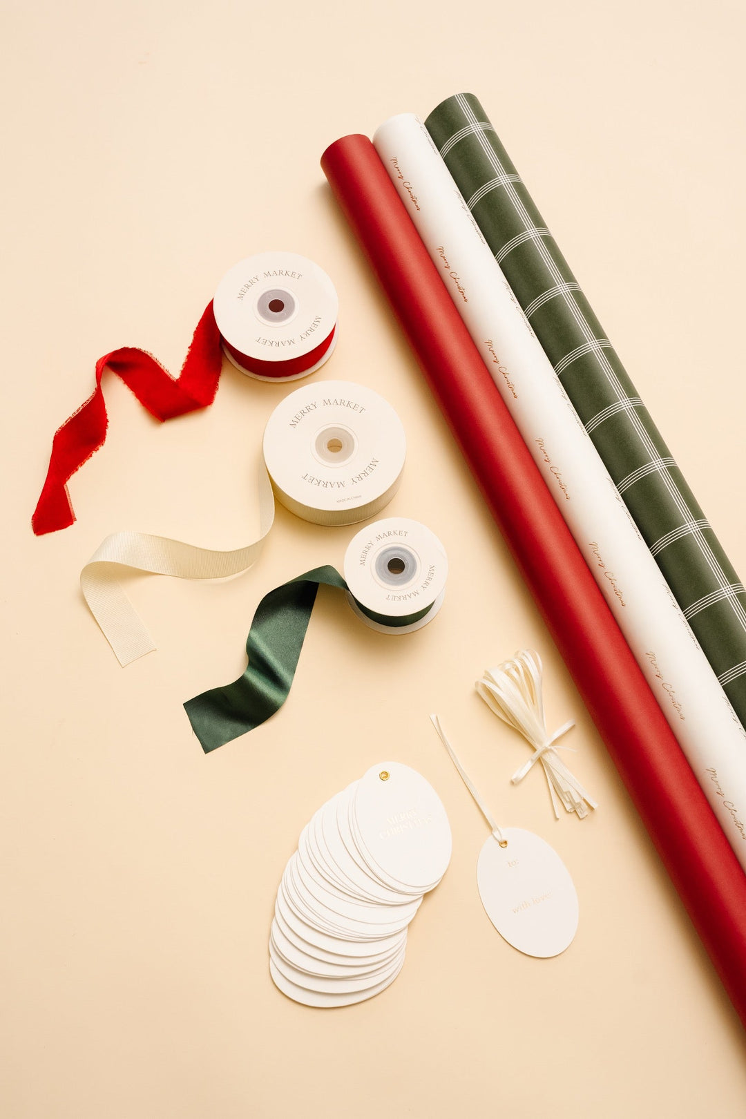 Gold foil Merry Christmas wrapping paper kit flat lay: three rolls, red, cream, and green ribbon, and oval tags