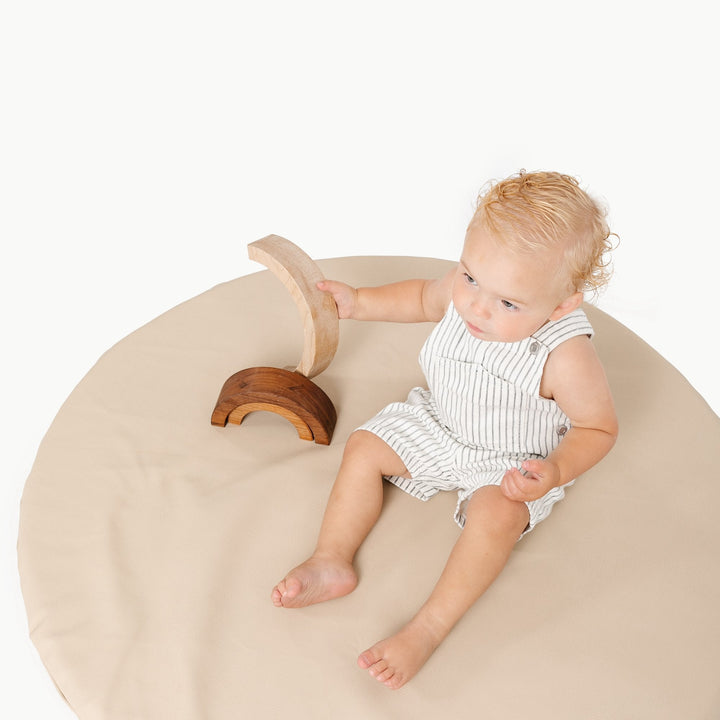 Toddler playing with a wooden rainbow stacker on the round Millet oatmeal padded play mat