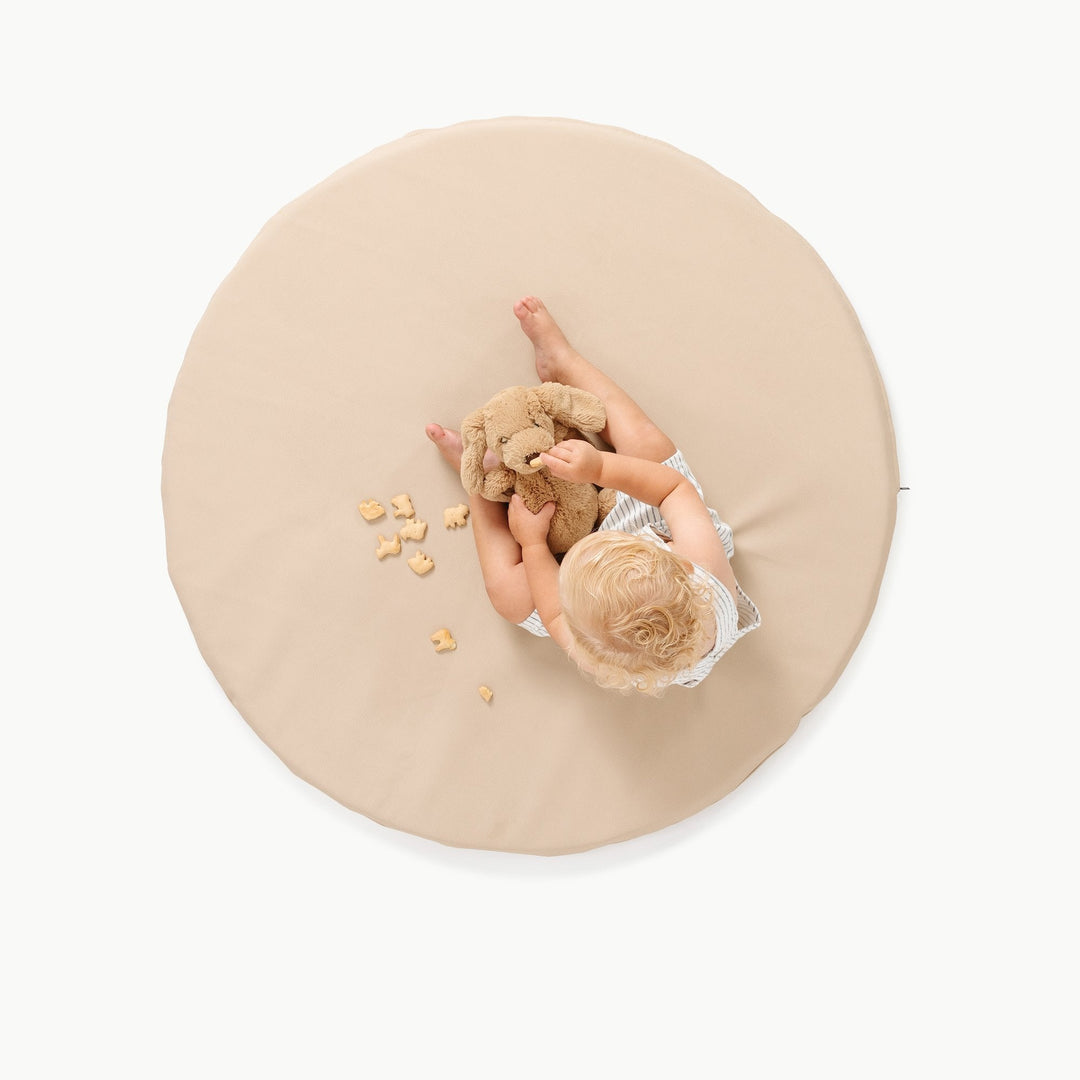 Overhead view of a toddler playing on the round Millet oatmeal padded play mat with a puppy plush