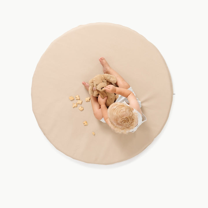 Overhead view of a toddler playing on the round Millet oatmeal padded play mat with a puppy plush