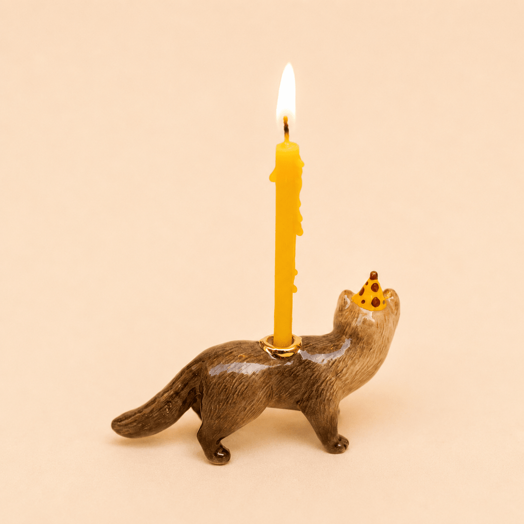 Porcelain mink cake topper seen from behind with a lit candle standing on its back