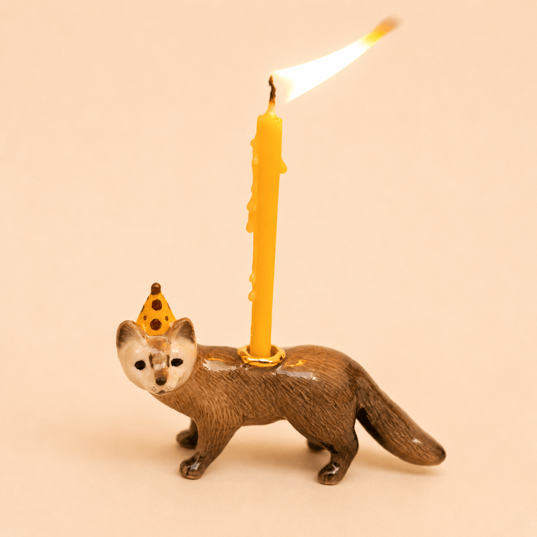 Mink cake topper walking pose with a tall lit beeswax candle on a warm backdrop