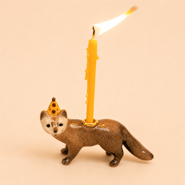Mink cake topper walking pose with a tall lit beeswax candle on a warm backdrop