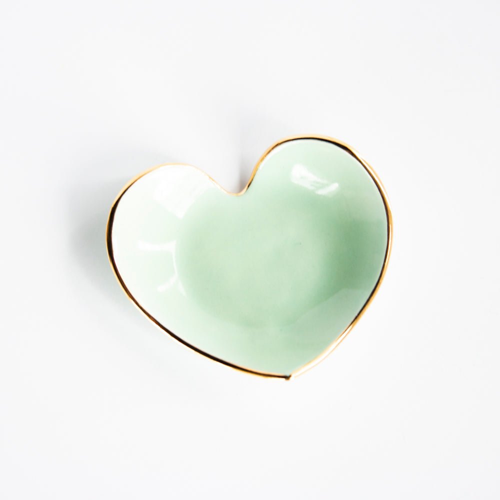 Mint green heart ring dish with a gold rim, top view on white