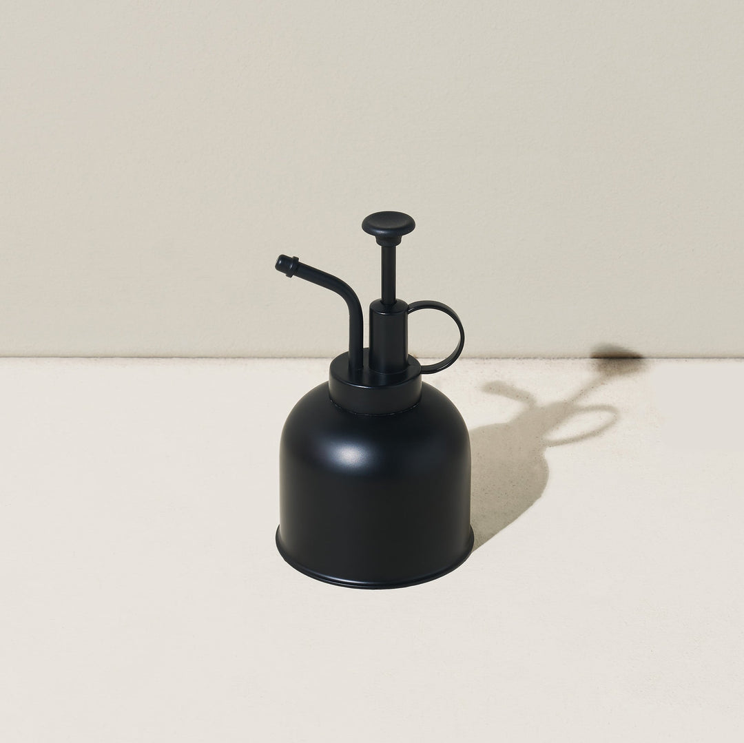 Matte black plant mister with a black pump and curved nozzle on a neutral backdrop