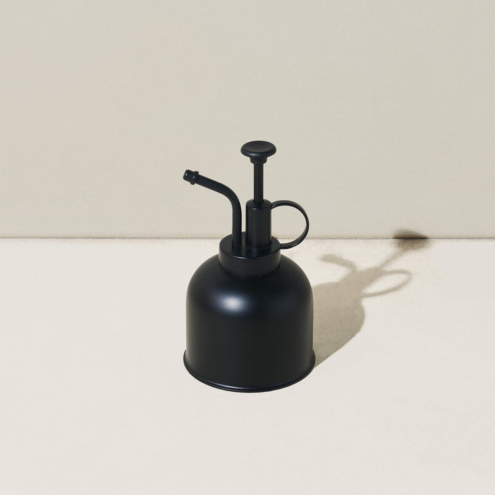 Matte black plant mister with a black pump and curved nozzle on a neutral backdrop