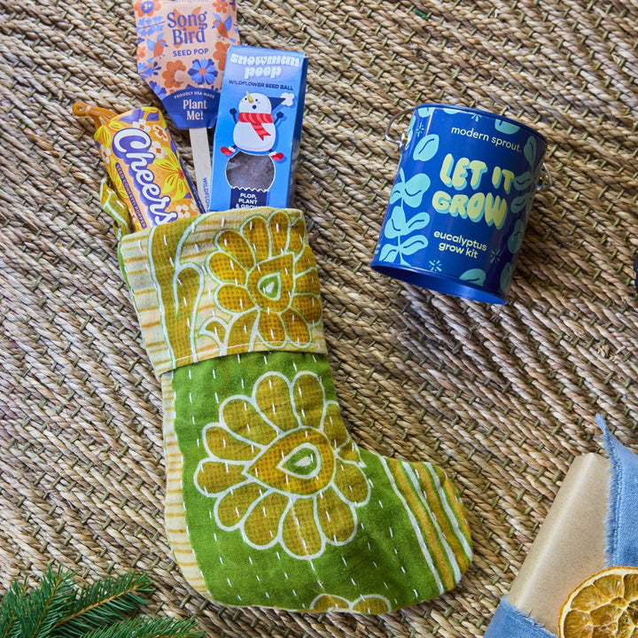 Blue Snowman Poop seed bomb box tucked into a green floral stocking beside a blue eucalyptus grow kit tin