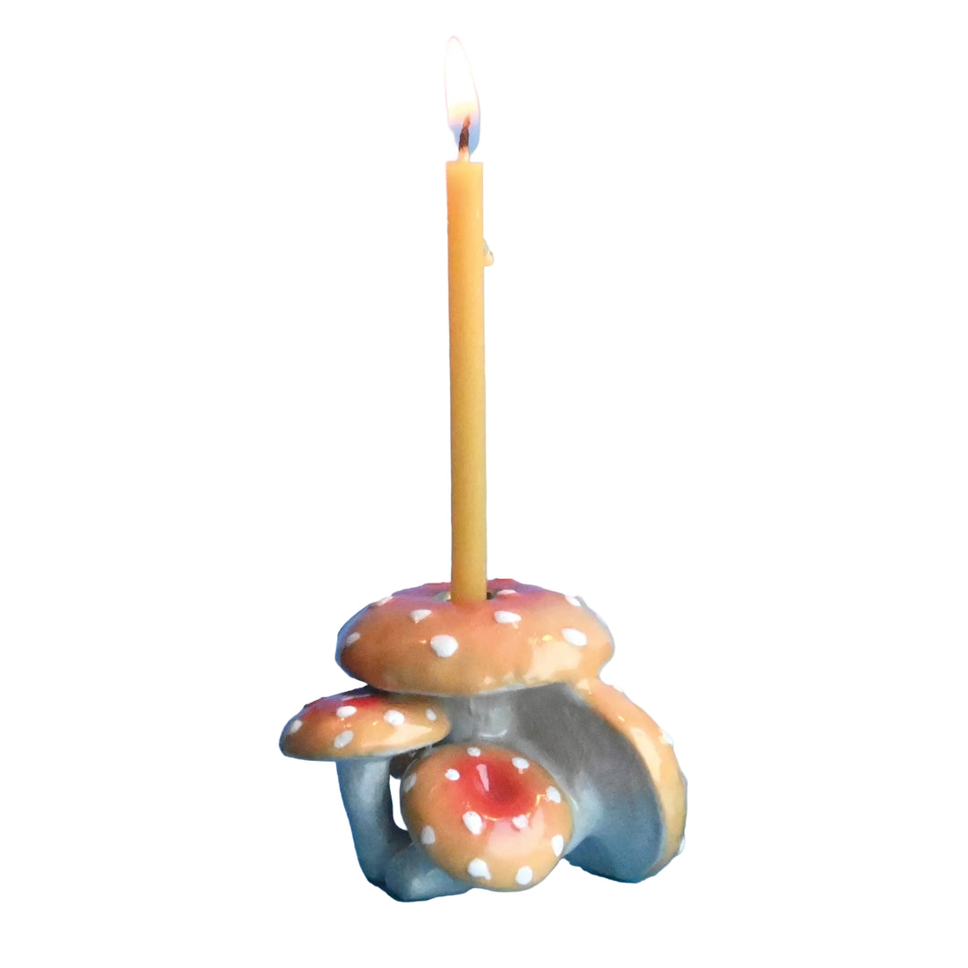 Orange spotted mushroom cluster porcelain candle holder with a lit birthday candle for a woodland or fairy party cake