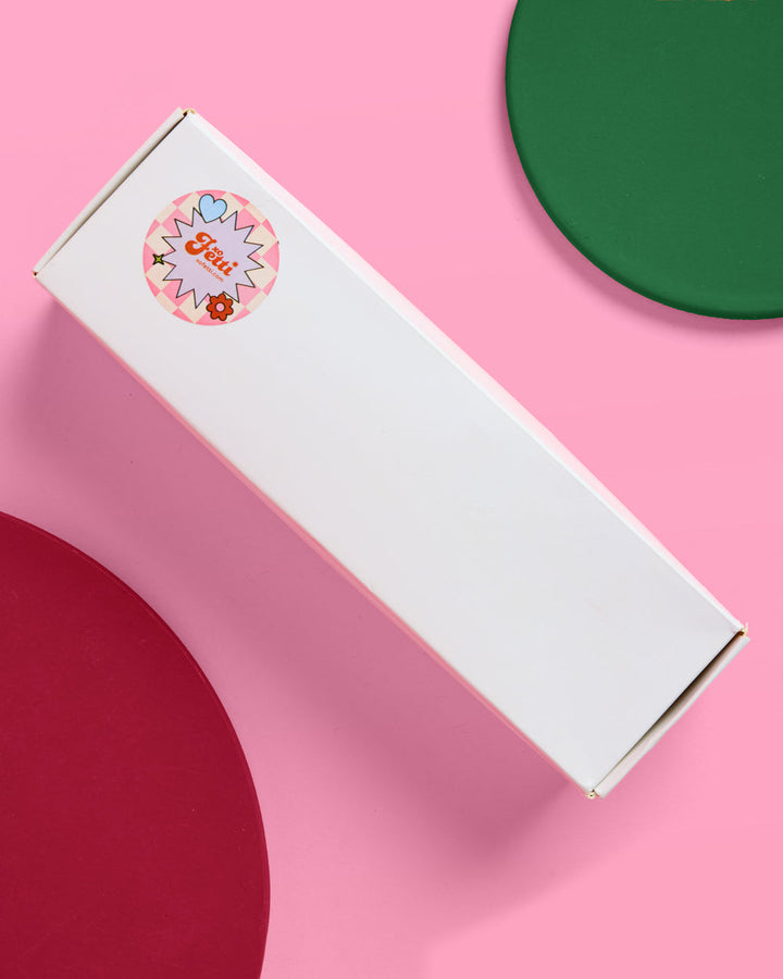 White gift box packaging for the mini martini ornament set on a pink background with red and green accents