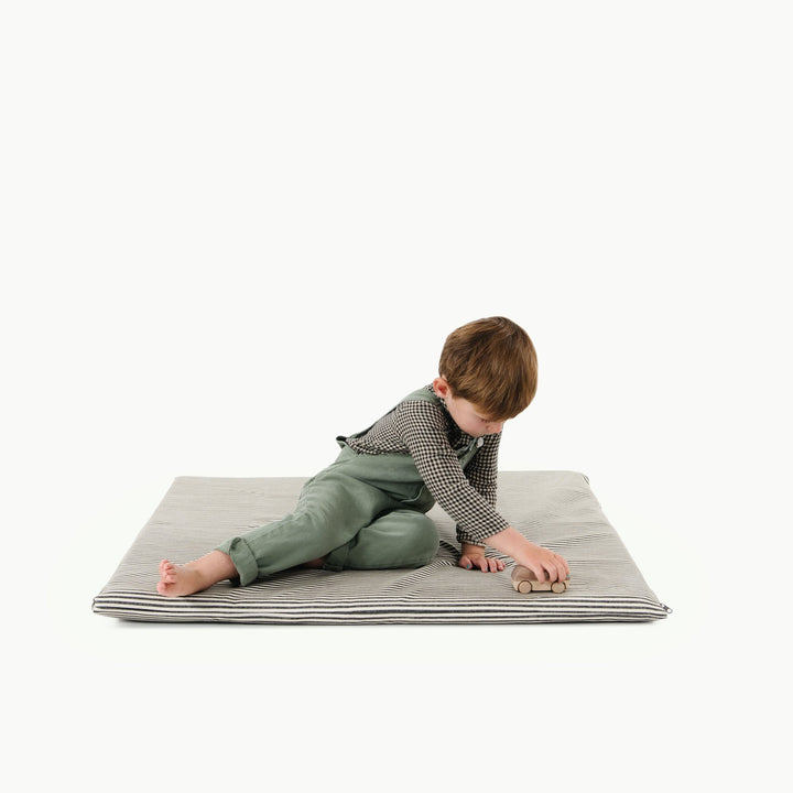 Black and white stripe padded baby play mat with a toddler playing with a wooden car.
