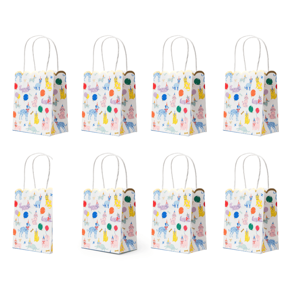 Eight small white gift bags arranged in two rows of four, each printed with a colorful whimsical pattern of balloons, animals, and decorative motifs, with white twisted paper handles.