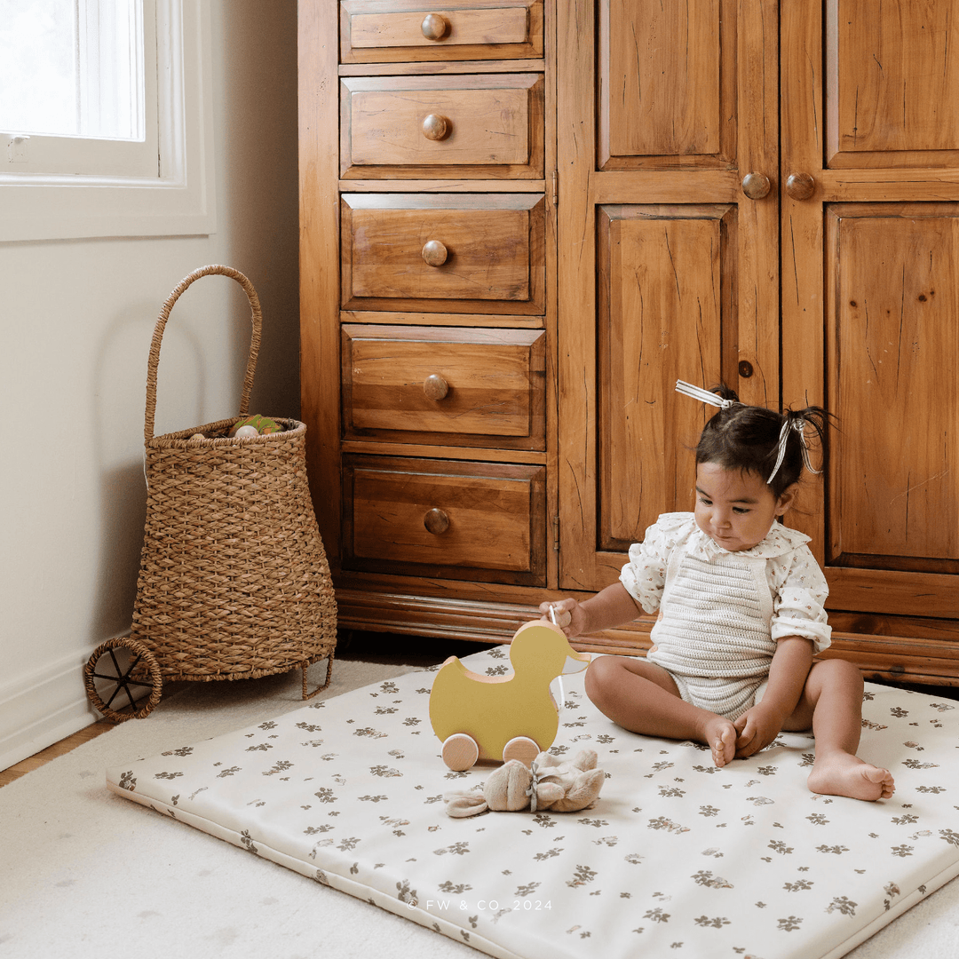 Baby playing in a nursery on the floral Peter Rabbit padded play mat with a wooden duck pull toy