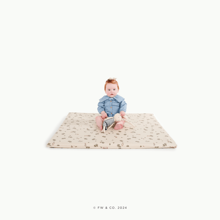 Baby sitting on the square Peter Rabbit padded play mat with a bunny plush