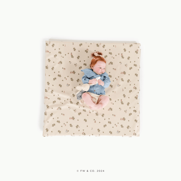Overhead view of a baby lying on the square Peter Rabbit padded play mat with a bunny plush