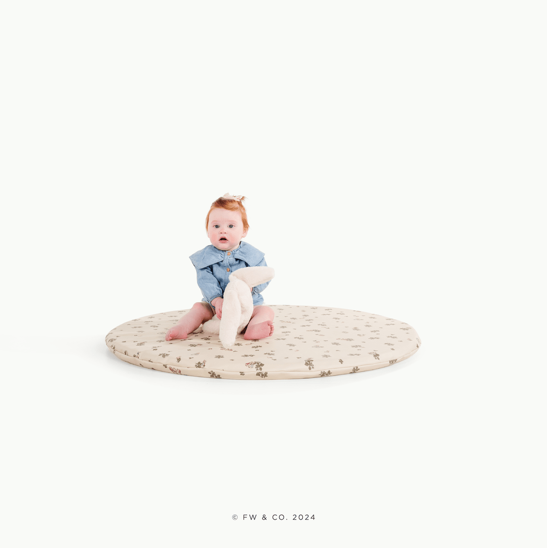 Baby sitting on the round Peter Rabbit padded play mat holding a bunny plush