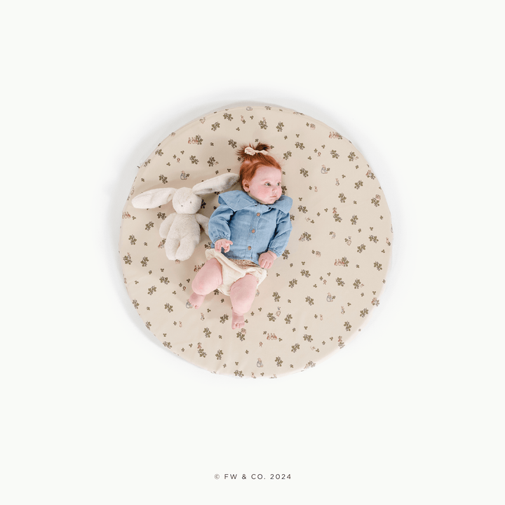 Overhead view of a baby lying on the round Peter Rabbit padded play mat with a bunny plush