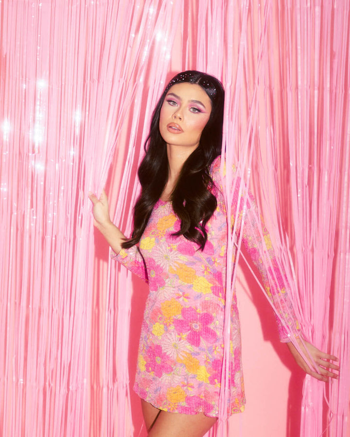Model in a floral dress standing in front of a matte pink fringe curtain photo backdrop