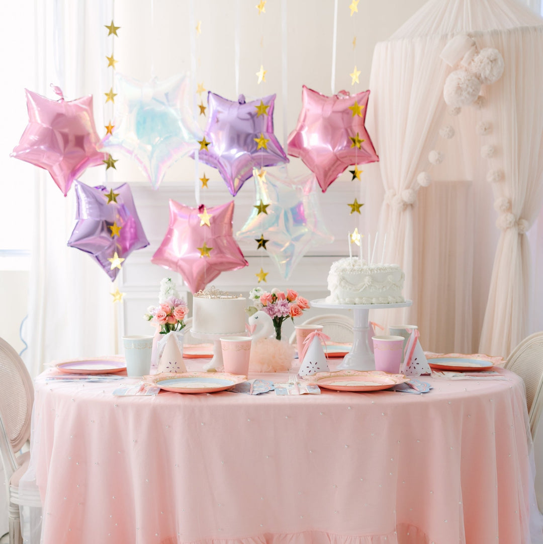 Princess birthday party table with a pink ruffled tablecloth, pink and lavender star balloons, a white layer cake, and a plush swan beside the table