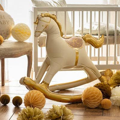 Cream and gold rocking horse balloon in a nursery beside a white crib with gold honeycomb decorations