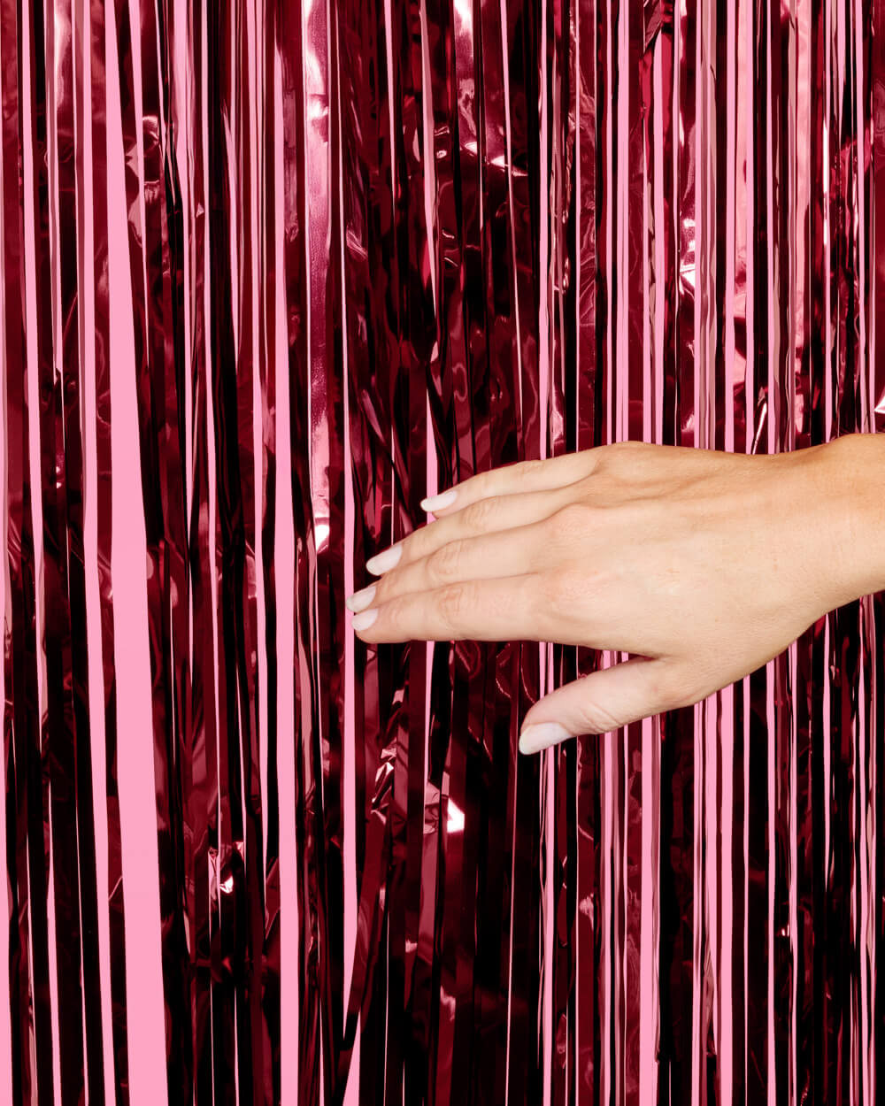 Hand parting the strands of a burgundy foil fringe curtain to show the layered cut