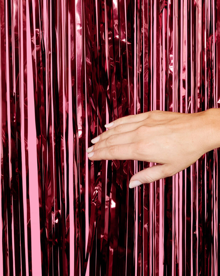 Hand parting the strands of a burgundy foil fringe curtain to show the layered cut