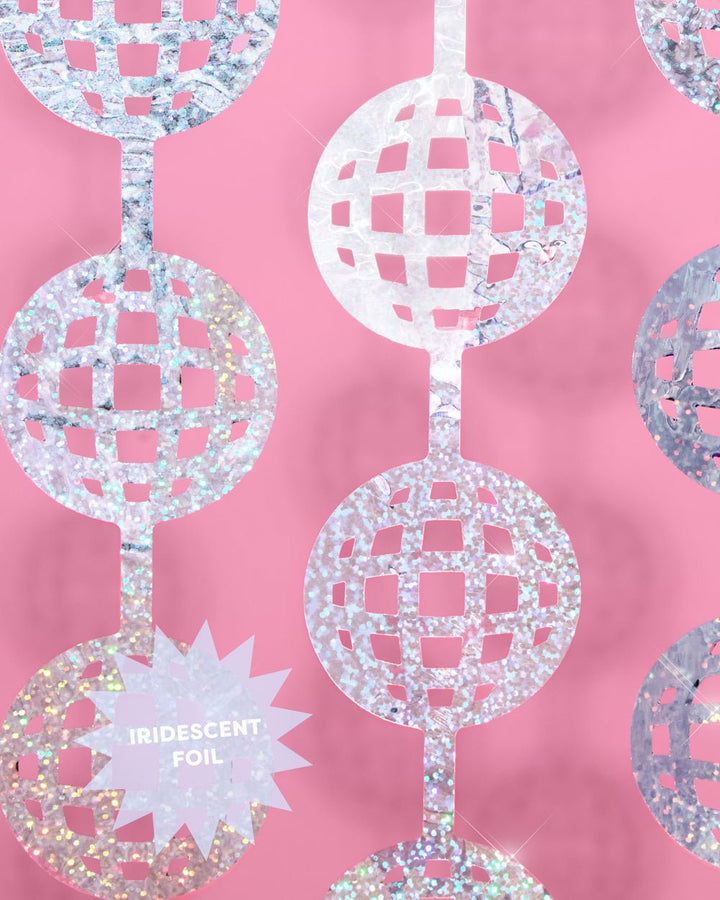 Close-up of a laser cut silver disco ball cutout labeled iridescent foil on a pink wall
