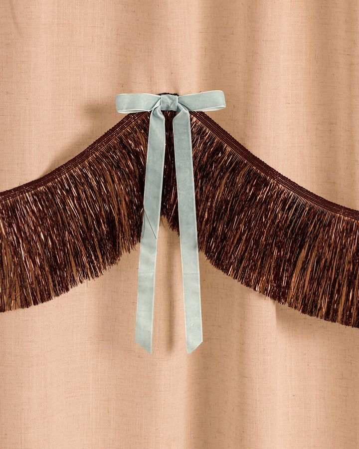 Close-up of brown metallic fringe and a hand-tied light blue velvet bow on the coquette party backdrop