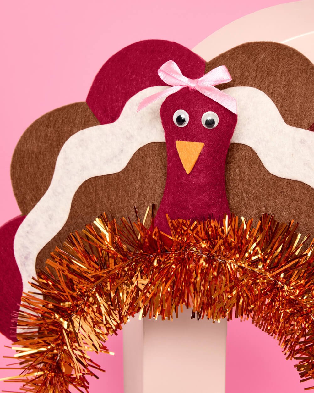 Close view of the turkey headband's googly eyes, orange beak, and pale pink bow