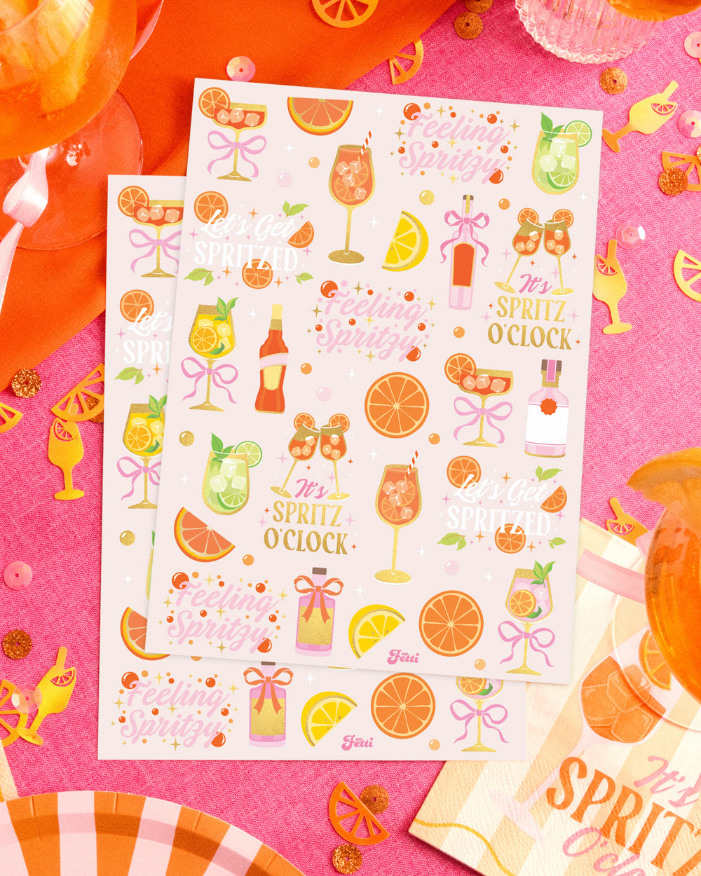 Two sheets of spritz temporary tattoos on a styled cocktail table with oranges and confetti