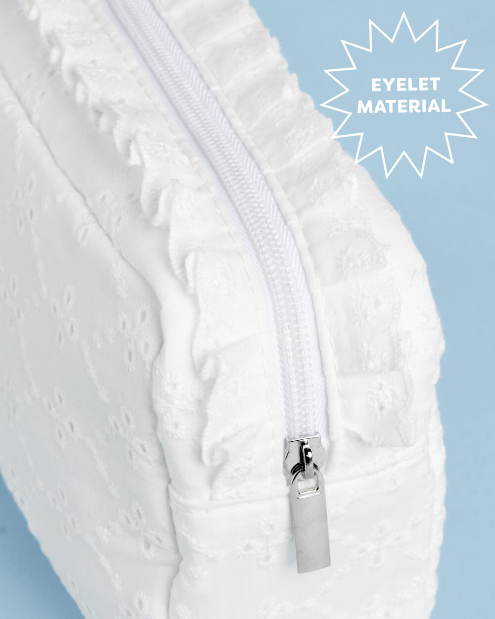 Close-up of the white eyelet cosmetic bag zipper, ruffled trim, and embroidered fabric texture.