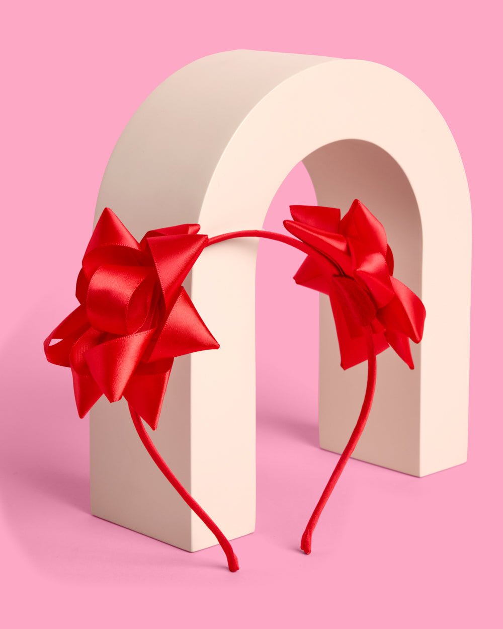 Red bow headband draped over a cream arch, showing both satin bows from the front