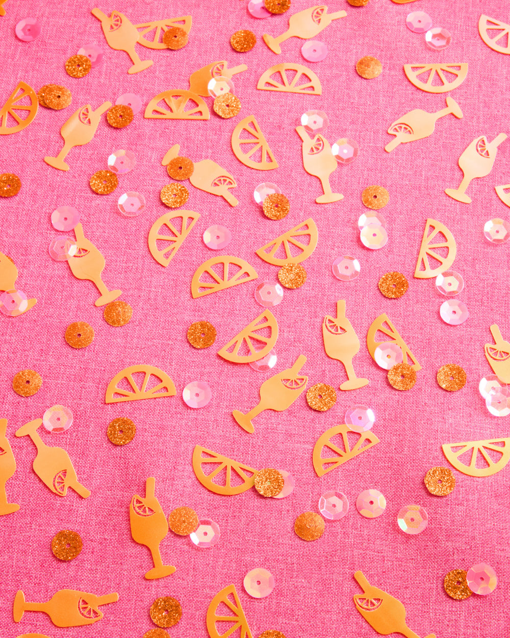 Spritz confetti on pink linen with orange slices, cocktail glasses, and iridescent pink sequins