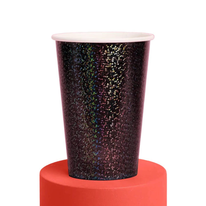 Single black iridescent speckled paper party cup on an orange riser