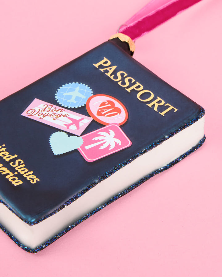 Another view of the Bon Voyage passport ornament, showing the travel sticker artwork across the navy glass cover.