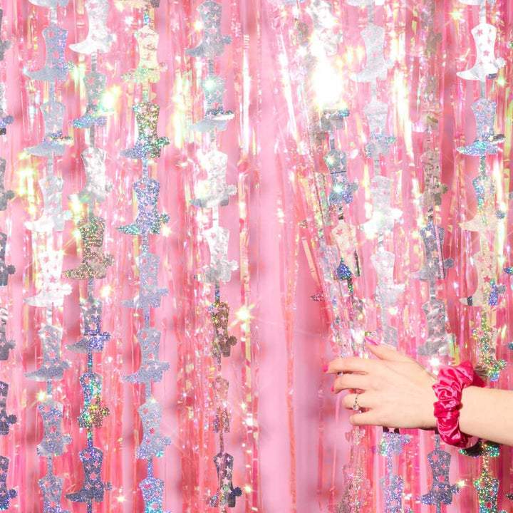 Hand parting the pink fringe and cowboy boot strand curtain, a fun photo backdrop for a rodeo party