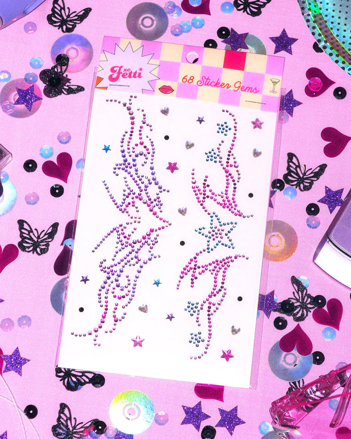 Purple and pink tribal-style Y2K body gem sheet on a pink table with butterfly confetti and CDs