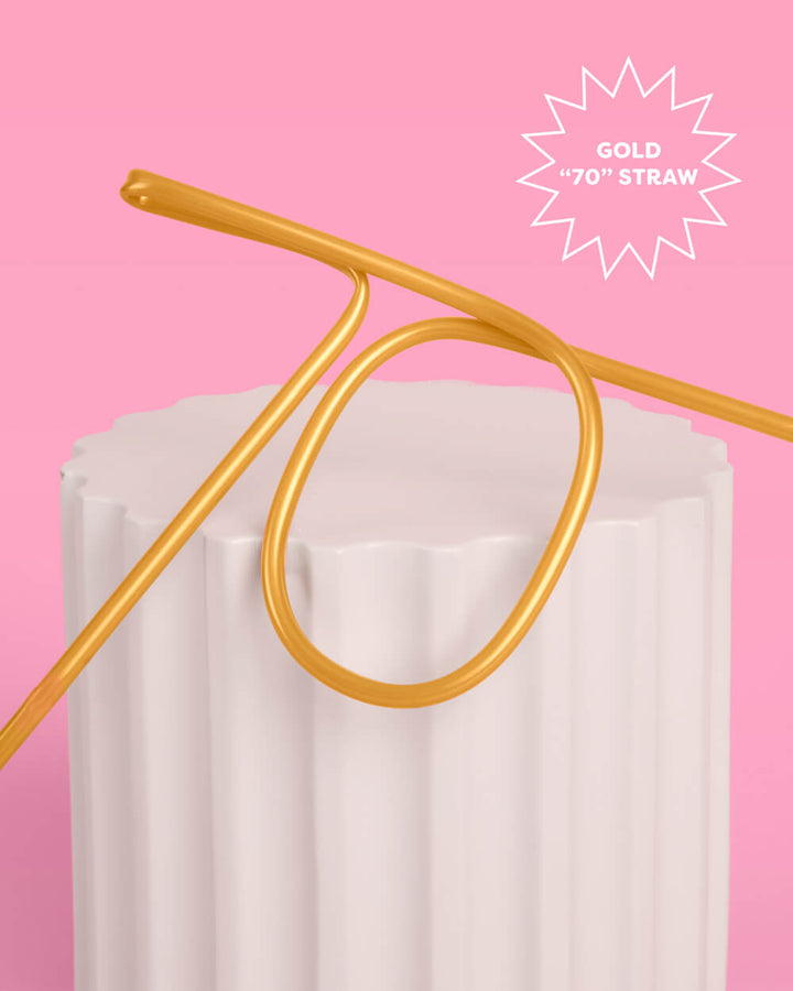 Gold 70th birthday straw resting against a white pedestal