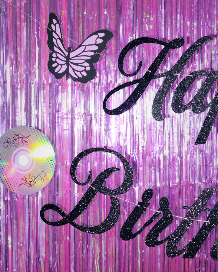 Black butterfly cutout and glitter Happy lettering on the Y2K birthday banner hung over shimmering purple fringe
