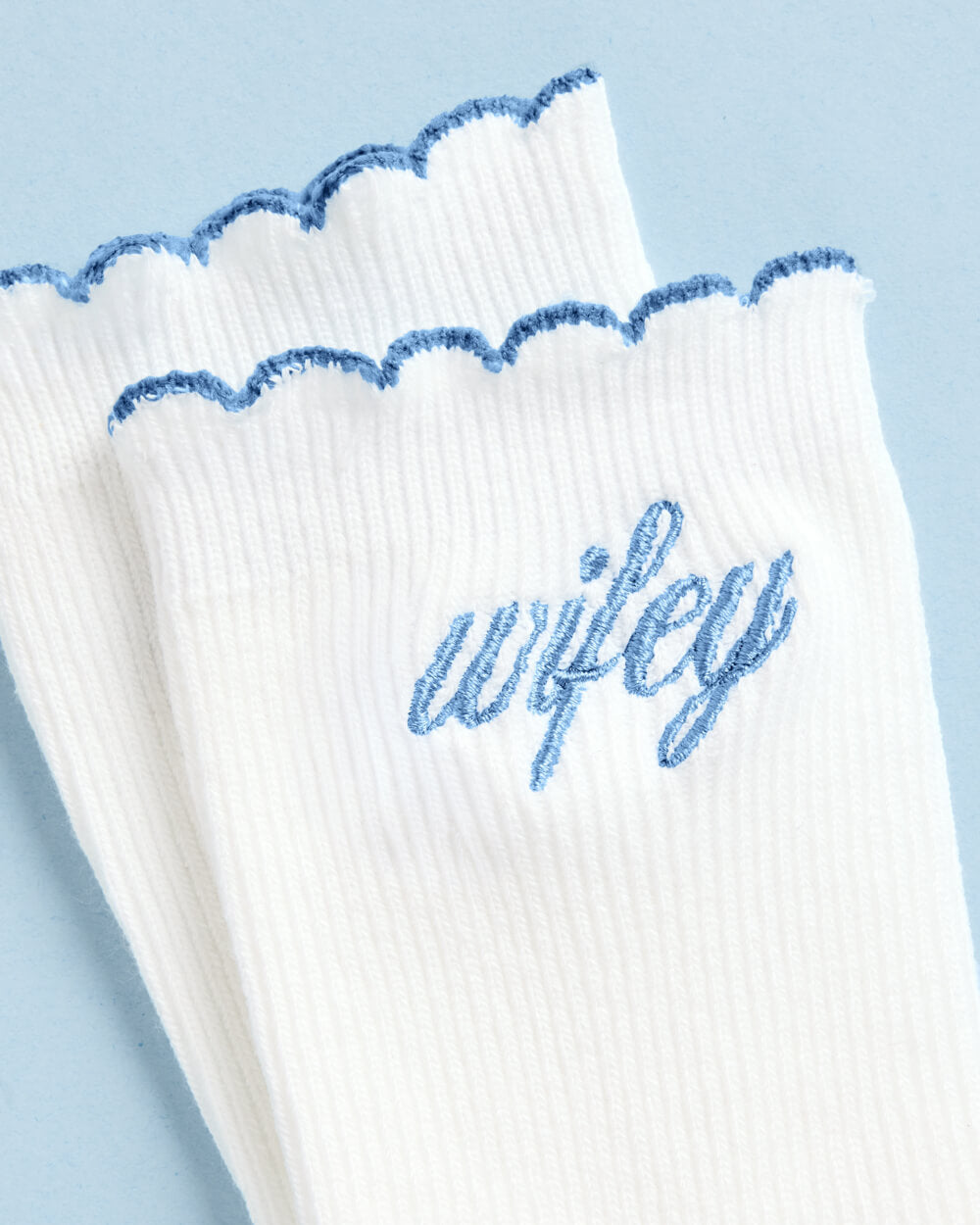 Close-up of light blue wifey embroidery and the scalloped blue edge on white crew sock cuffs